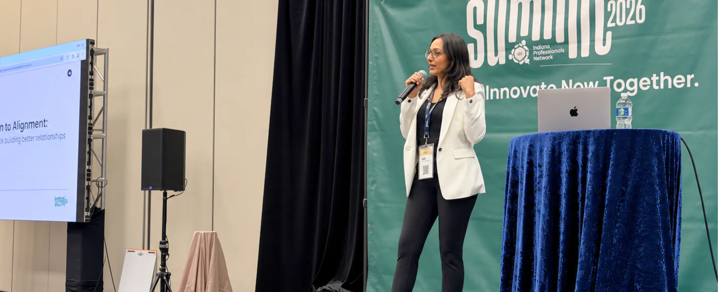 Dr. Naaila Chagani speaking on stage at the Ismaili Professionals Network Summit 2026, holding a microphone in front of the IPN Summit backdrop